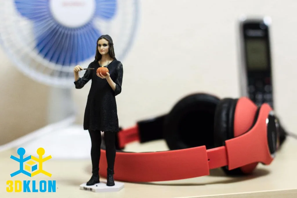 3D-фигурка девушки в черном платье с тыквой рядом с красными наушниками на столе