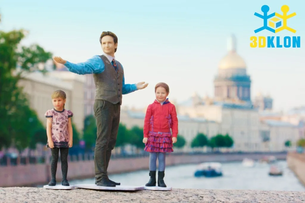 Цветные 3D-фигурки мужчины и двух девочек на каменном парапете у реки